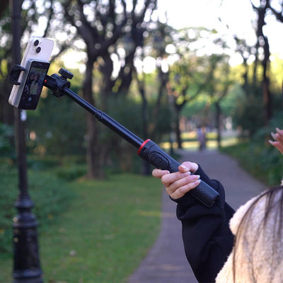 Person holding a selfie stick with a phone using the stravelle selfie monitor in a park setting